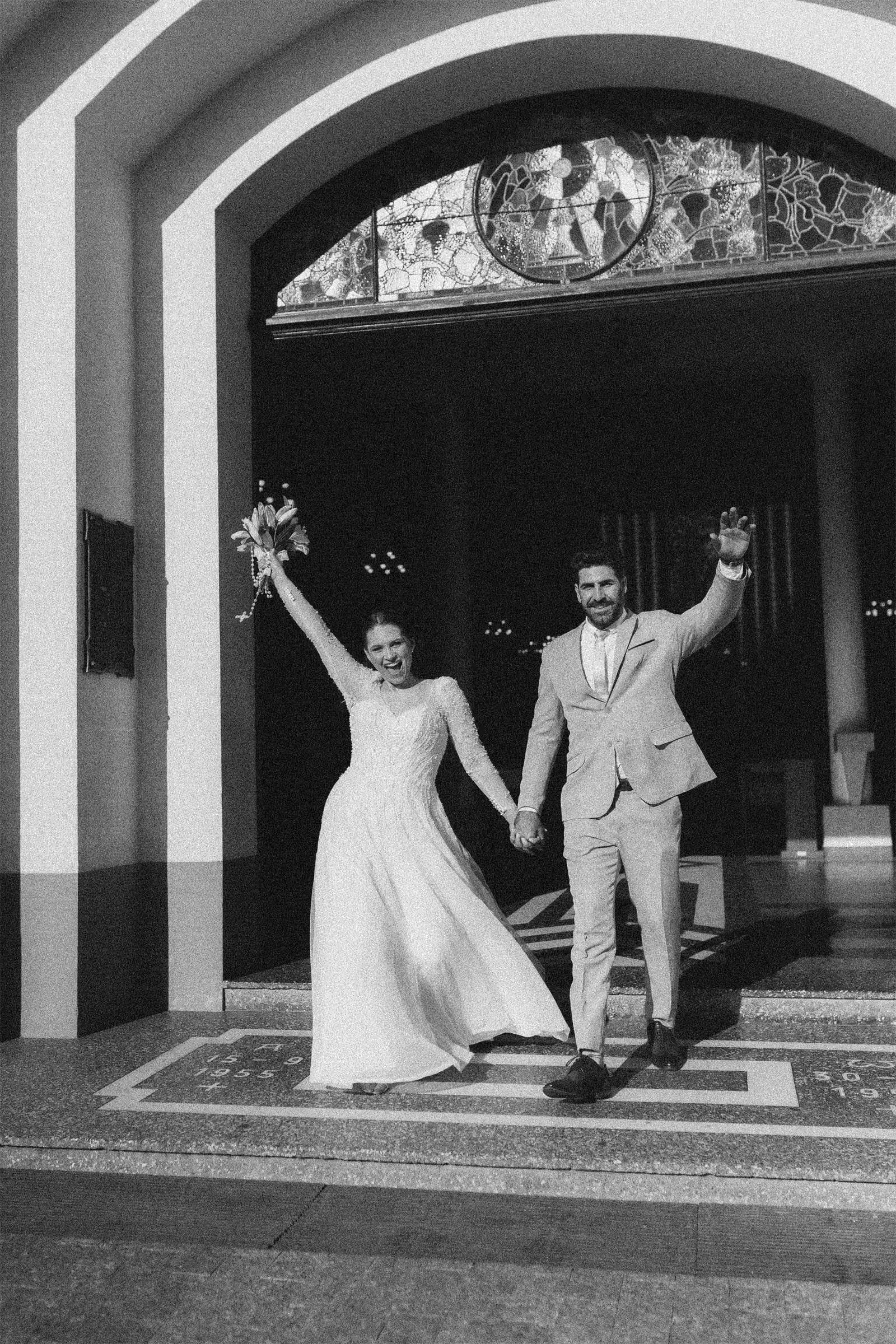 Recién casados celebrando con los brazos en alto al salir de la ceremonia